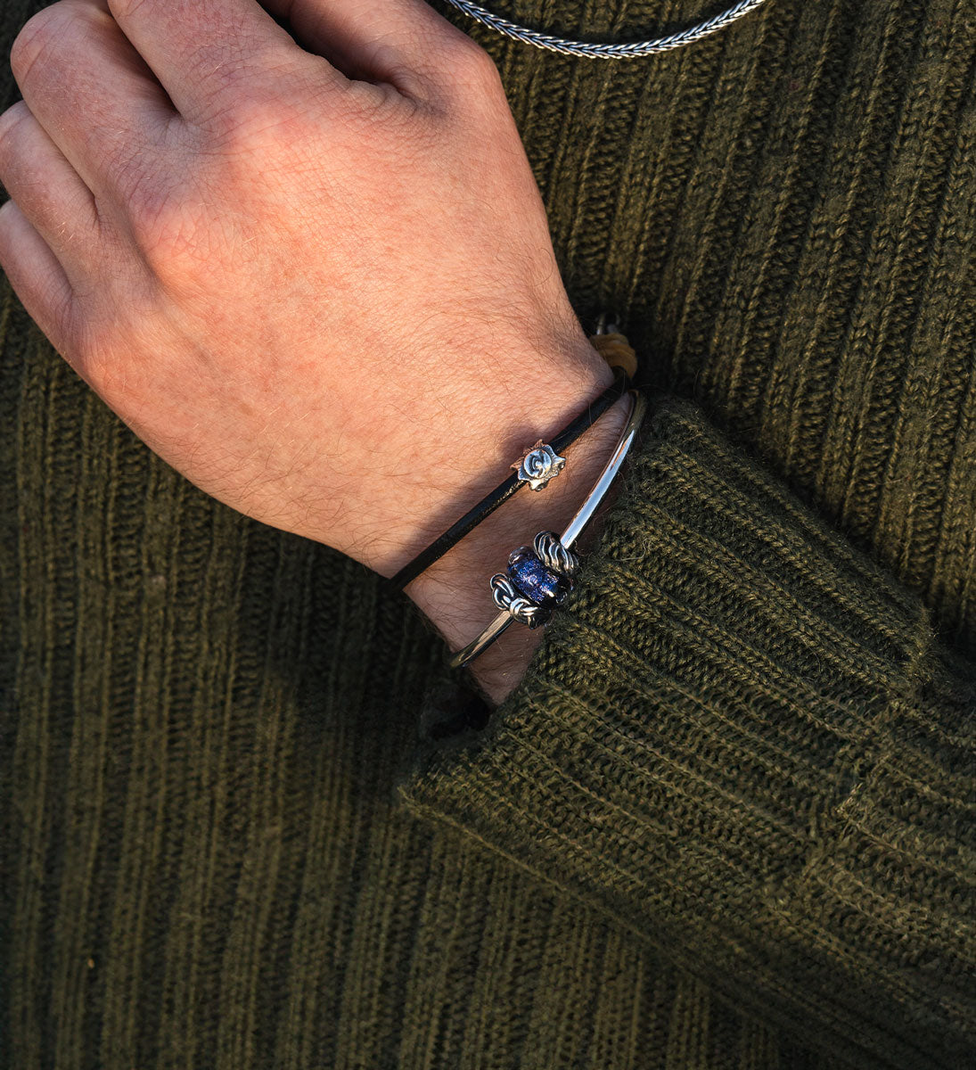 Trollbeads solskins sølvkugle på et læder armbånd komplimenteret  af en sølvarmring med blå glaskugle og to sølv spacers på en mandlig model iført en grøn sweater