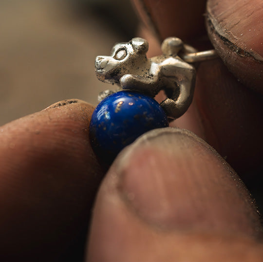 Smykkecharme af en hundefigur på en kugle af lapis lazuli, der er ved at blive fremstillet, viser indviklede detaljer og levende farver i en fængslende udstilling af håndværk